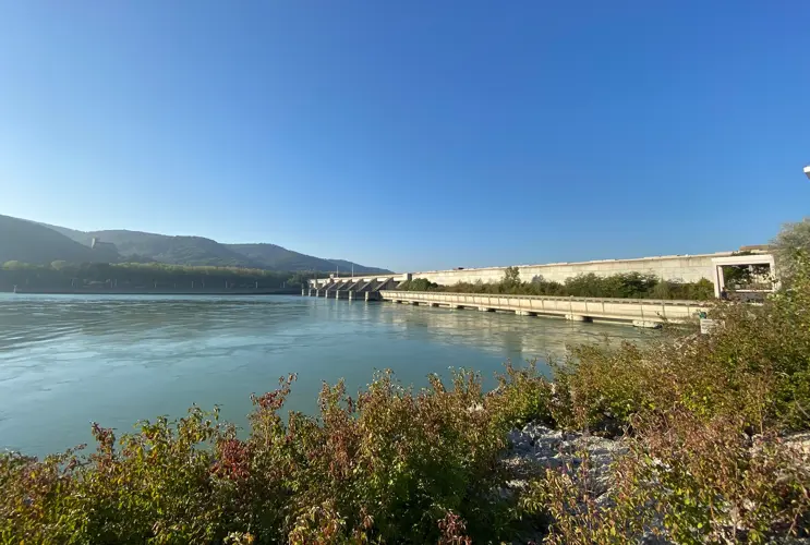 Wir blicken auf eine Wasserkraftwerk bei strahlend blauem Sonnenschein. Die Stimmung ist herbstlich.